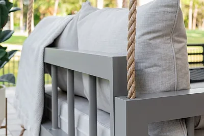 Close-up of the Connie swing bed gray frame arm, manila rope, and ivory cushions