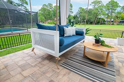 Debbie swing bed in white with a cane end panel and navy blue Sunbrella cushions beside a pool