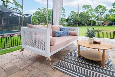 Debbie swing bed in white with a cane end panel, blush cushions, and navy blue pillows