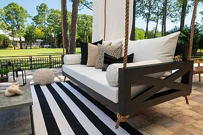 Charcoal swing bed with X-pattern end panel, white Sunbrella cushions, and a black and white striped outdoor rug