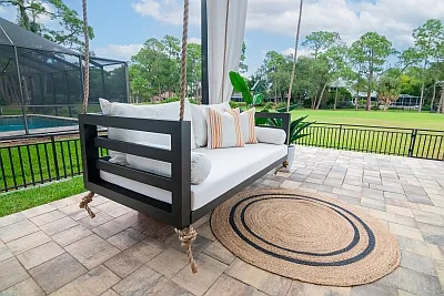 Shirley swing bed in bronze with white cushions, striped pillows, and a round jute rug