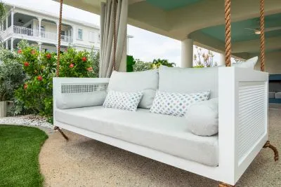 Debbie swing bed in white with ivory cushions and aqua print pillows beside a poolside cabana