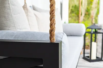 Close-up of the Maggie swing bed black frame, manila rope, and ivory cushions with a candle lantern