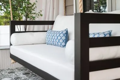 Close-up of the black Shirley swing bed with white cushions and a blue quatrefoil lumbar pillow