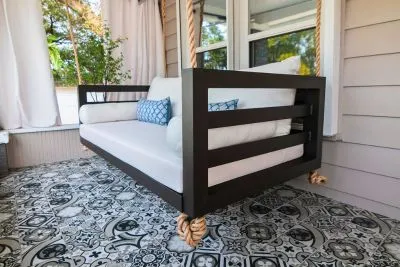 Shirley swing bed in black with white cushions on a porch with black and white patterned tile