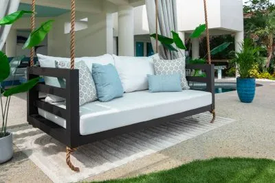 Shirley swing bed in black with white cushions and aqua blue accent pillows beside a pool