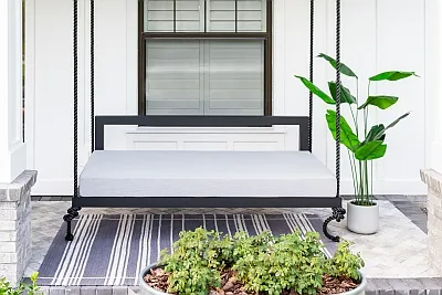 Front view of the Sophia swing bed in black with a gray mattress cushion and striped rug