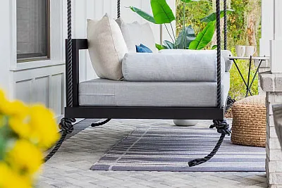 Sophia swing bed in black with gray cushions and ivory pillows on a porch with yellow flowers