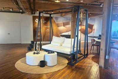 Sophia swing bed in black suspended from a freestanding swing stand with white cushions in a showroom