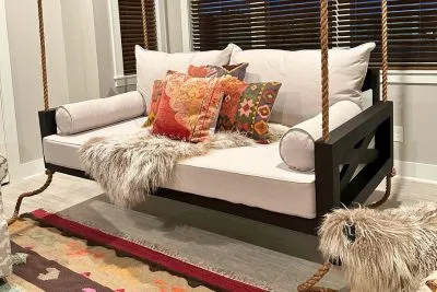 Maggie swing bed in black styled indoors with ivory cushions, boho floral pillows, and a faux fur throw