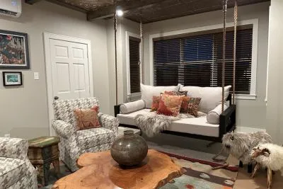 Black Maggie swing bed hung indoors in a living room with boho pillows, a patterned armchair, and a live-edge wood table